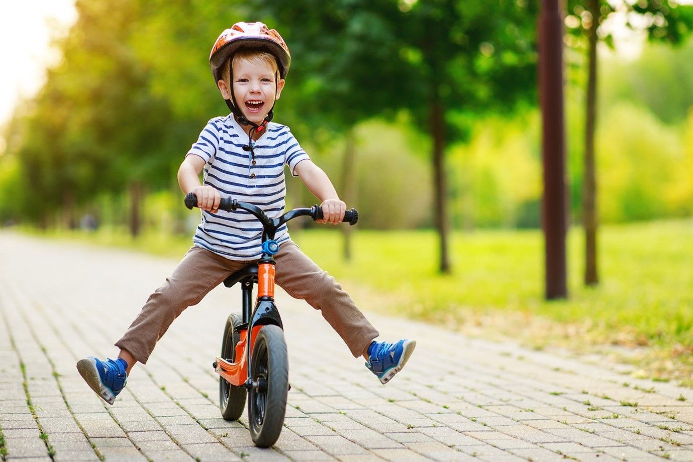 mały chłopiec w kasku jedzie na rowerku biegowym z nogami rozstawionymi na boki